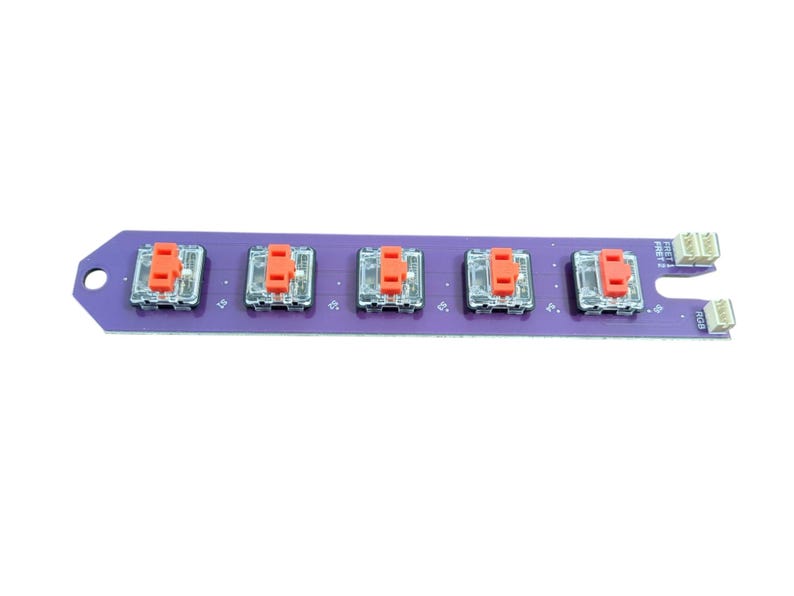 May include: A purple circuit board with five red and clear mechanical keyboard switches. The board has a small notch on the left side and a row of pins on the right side.