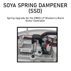 May include: Close-up of a white guitar controller component with a black spring dampener labeled "SOYA SPRING DAMPENER (SSD)". The text "Spring Upgrade for the CRKD LP Blueberry Burst Guitar Controller" is also visible.