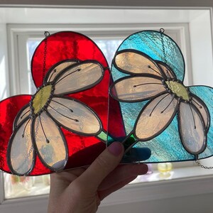 May include: Two stained glass hearts with a daisy design. One heart is red and the other is blue.