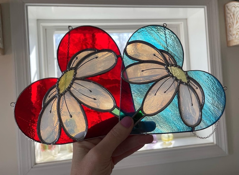 May include: Two stained glass hearts with a daisy design. One heart is red and the other is blue.