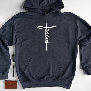 May include: A dark gray hooded sweatshirt with a white cross and the word "Jesus" written vertically on it.