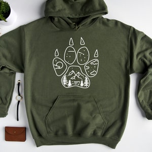 May include: A dark green hooded sweatshirt with a white paw print design. The paw print features a mountain scene with trees, clouds, and stars.