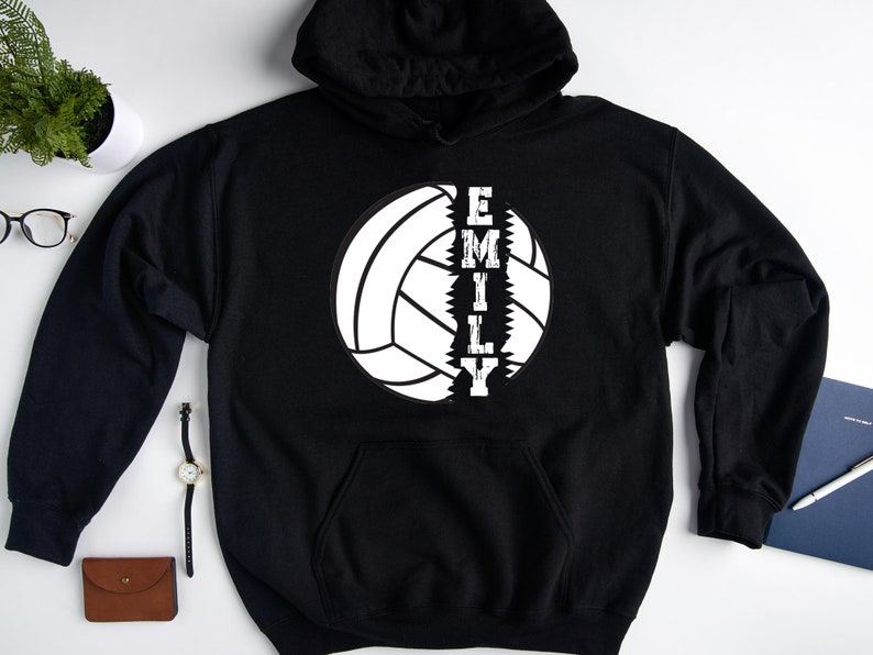 May include: Black hoodie with a white volleyball graphic and the word "EMILY" written vertically down the side of the ball.