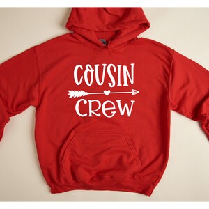 May include: Red hooded sweatshirt with a white graphic that says "COUSIN CREW" with an arrow and a heart.