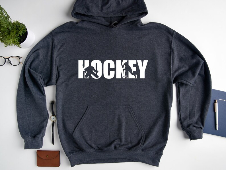 May include: A dark gray hooded sweatshirt with the word "HOCKEY" printed in white on the front. The word is made up of hockey players in silhouette.