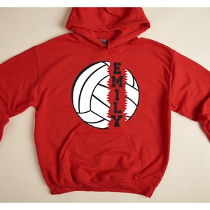 May include: Red hooded sweatshirt with a white volleyball graphic and the name "EMILY" printed vertically down the side of the ball.