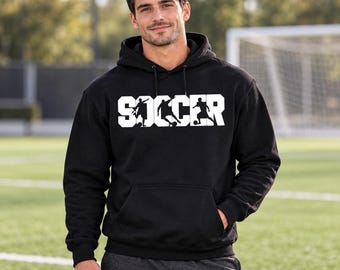 May include: A black hooded sweatshirt featuring the word SOCCER printed in large white block letters across the chest. The letters incorporate silhouettes of players in action poses with a ball. The hoodie includes a front kangaroo pocket.