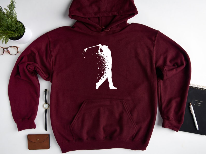 Op de afbeelding: Bordeauxkleurige hoodie met een wit silhouet van een golfer die een club zwaait. De golfer is gemaakt van verspreide witte stippen.