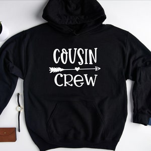 May include: Black hooded sweatshirt with white text that reads "COUSIN CREW" with an arrow and heart graphic.