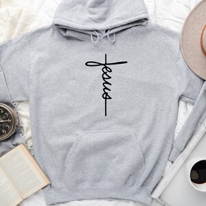 May include: A gray hooded sweatshirt with a black cross and the word "Jesus" written vertically on it.