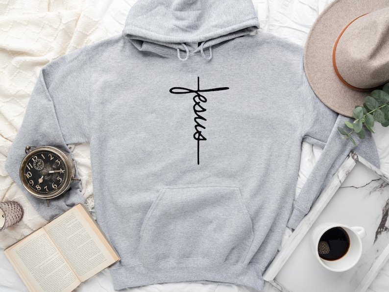 May include: A gray hooded sweatshirt with a black cross and the word "Jesus" written vertically on it.