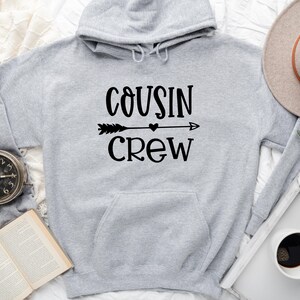 May include: Gray hooded sweatshirt with the text "COUSIN CREW" in black lettering with an arrow and heart graphic.