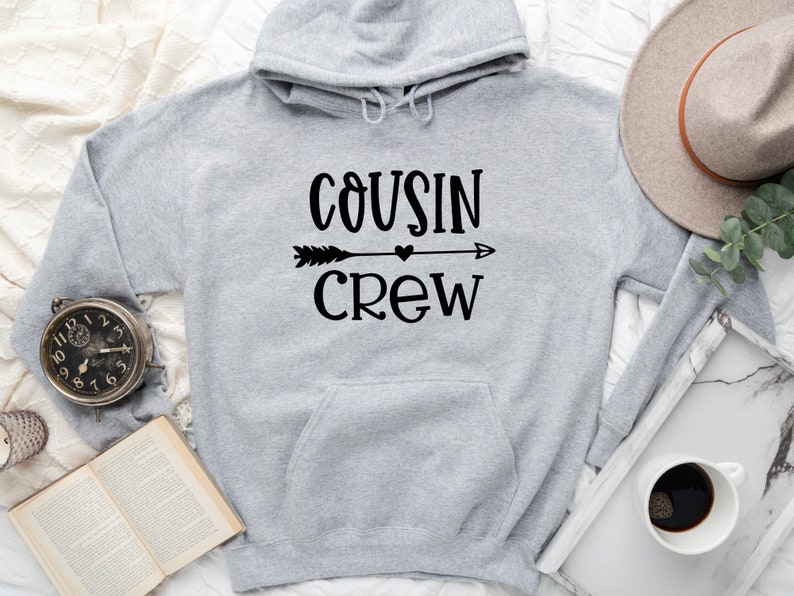 May include: Gray hooded sweatshirt with the text "COUSIN CREW" in black lettering with an arrow and heart graphic.
