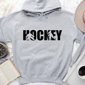May include: Gray hooded sweatshirt with the word "HOCKEY" printed in black with a hockey player silhouette on each side of the word.