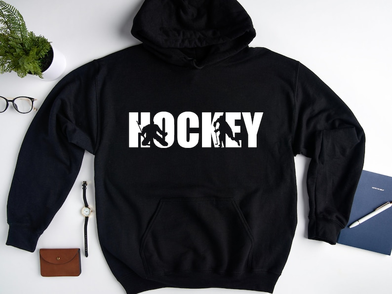 May include: Black hoodie with a white graphic of two hockey players and the word "HOCKEY" in white letters.