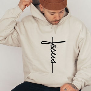 May include: A beige hoodie with a black cross and the word "Jesus" written vertically on it.