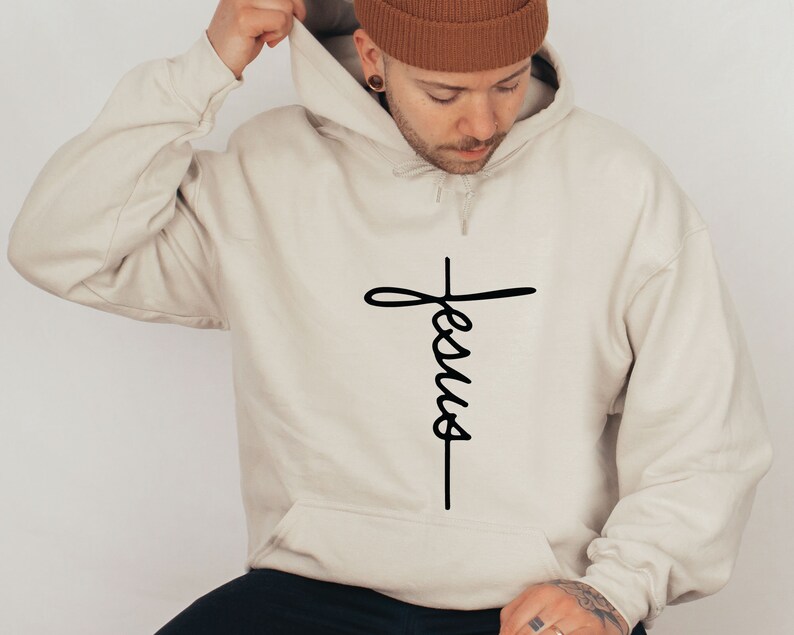 May include: A beige hoodie with a black cross and the word "Jesus" written vertically on it.