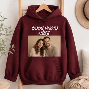 May include: A maroon long-sleeve hooded sweatshirt featuring a front kangaroo pocket and a rectangular graphic print of a smiling couple. Above the photograph, the white text reads "YOUR PHOTO HERE" in a casual, handwritten-style font.