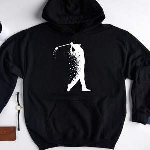 Op de afbeelding: Zwart hoodie met een wit silhouet van een golfer die een club zwaait. De golfer is gemaakt van verspreide witte stippen.