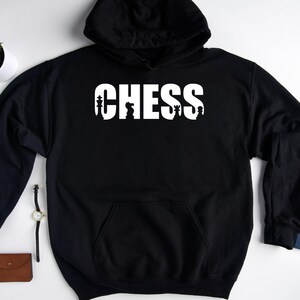 以下が含まれることがあります： チェスの駒が文字に組み込まれた「CHESS」という白いグラフィックが施された黒いフード付きスウェットシャツです。