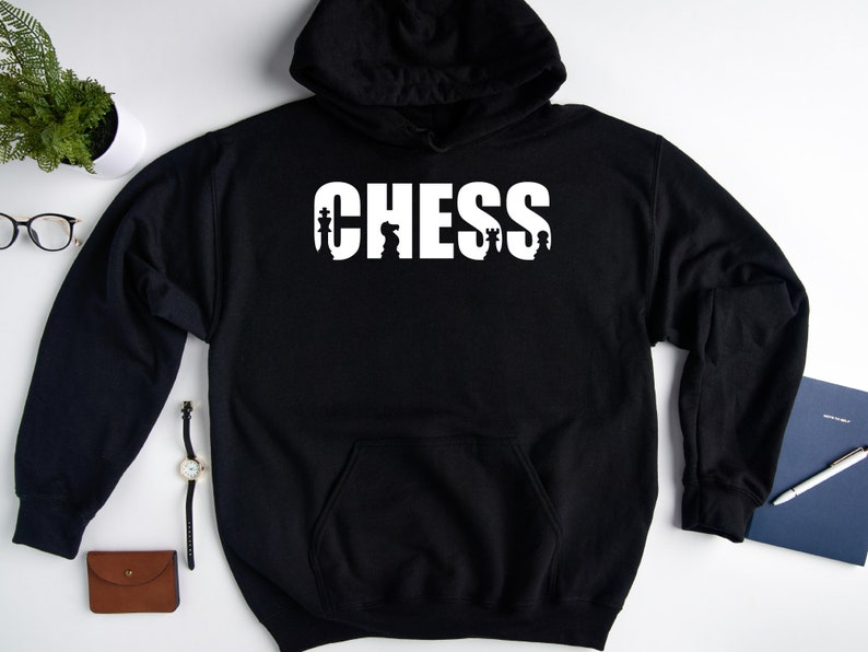 以下が含まれることがあります： チェスの駒が文字に組み込まれた「CHESS」という白いグラフィックが施された黒いフード付きスウェットシャツです。