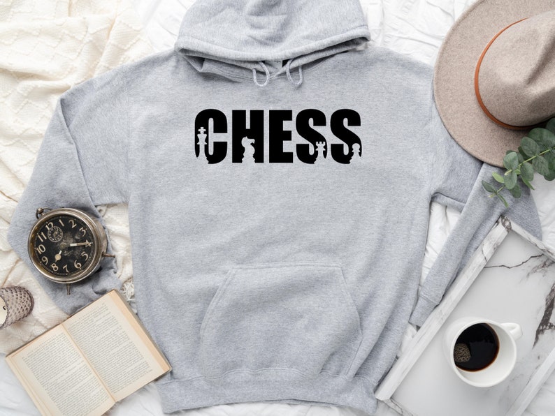 以下が含まれることがあります： グレーのフード付きスウェットシャツで、前面に黒で「CHESS」とプリントされています。単語は、黒いチェスの駒のシルエットで囲まれています。
