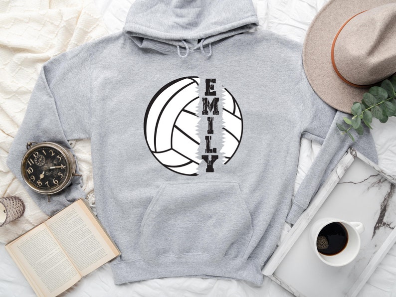 May include: Gray hooded sweatshirt with a white volleyball graphic and the name "EMILY" printed vertically down the side of the volleyball.