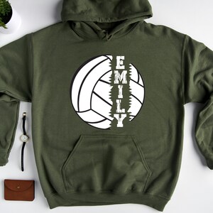May include: A green hooded sweatshirt with a white volleyball graphic and the word "EMILY" printed vertically down the side of the volleyball.