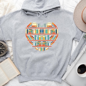 K&ouml;nnte beinhalten: Ein grauer Hoodie mit einem herzf&ouml;rmigen Design aus bunten B&uuml;chern. Das Design befindet sich mittig auf der Vorderseite des Hoodies.