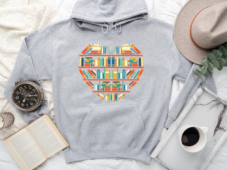 K&ouml;nnte beinhalten: Ein grauer Hoodie mit einem herzf&ouml;rmigen Design aus bunten B&uuml;chern. Das Design befindet sich mittig auf der Vorderseite des Hoodies.