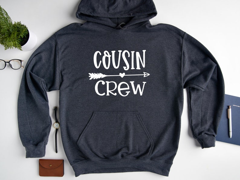 May include: A dark gray hooded sweatshirt with the text "COUSIN CREW" in white lettering. An arrow with a heart in the middle is above the word "CREW".