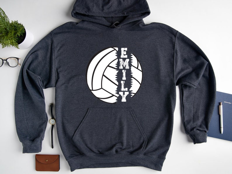 May include: A dark gray hooded sweatshirt with a white volleyball graphic and the name "EMILY" printed vertically down the center of the volleyball.