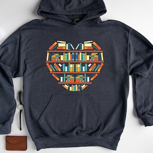 K&ouml;nnte beinhalten: Ein dunkelgrauer Kapuzenpullover mit einem grafischen Design eines herzf&ouml;rmigen B&uuml;cherregals, das mit bunten B&uuml;chern gef&uuml;llt ist.