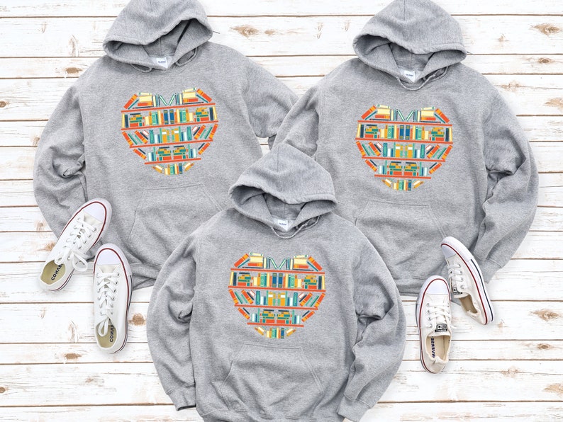 K&ouml;nnte beinhalten: Drei graue Kapuzenpullover mit einem bunten Herzdesign aus B&uuml;chern. Das Herzdesign enth&auml;lt den Text "Ich liebe B&uuml;cher".