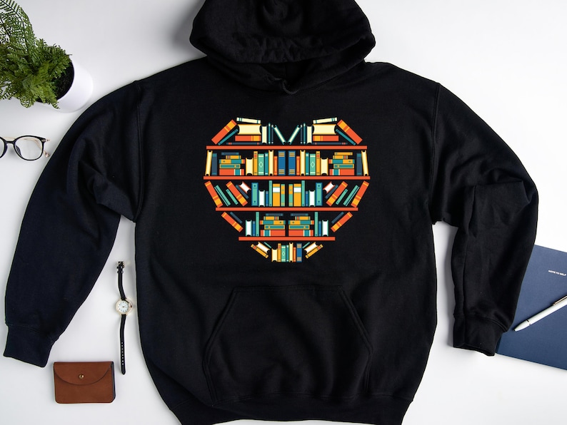K&ouml;nnte beinhalten: Schwarzer Kapuzenpullover mit einem Grafikdruck eines Herzens aus B&uuml;chern in einem B&uuml;cherregal.