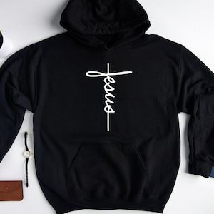 May include: Black hooded sweatshirt with a white cross and the word "Jesus" written vertically on it.
