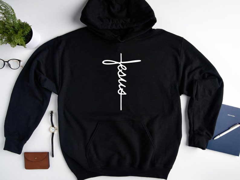 May include: Black hooded sweatshirt with a white cross and the word "Jesus" written vertically on it.