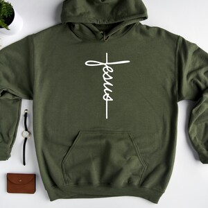 May include: A green hooded sweatshirt with a white cross and the word "Jesus" written vertically on it.