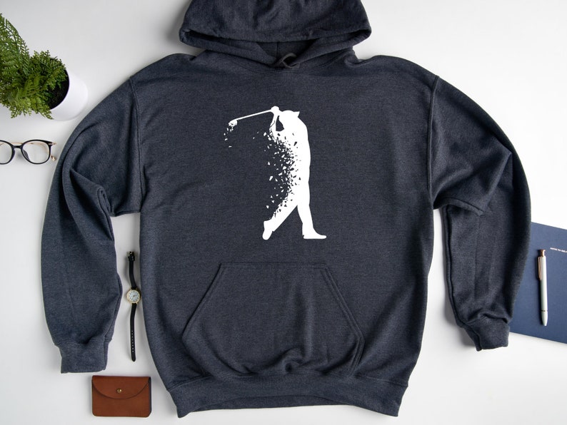 Op de afbeelding: Een donkergrijs hoodie met een wit silhouet van een golfer die een club zwaait. Het silhouet is gemaakt van kleine witte stippen.