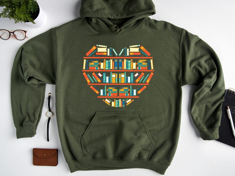 K&ouml;nnte beinhalten: Ein gr&uuml;ner Kapuzenpullover mit einem Grafikdruck eines Herzens aus B&uuml;chern in einem B&uuml;cherregal. Die B&uuml;cher sind in verschiedenen Farben und Gr&ouml;&szlig;en.