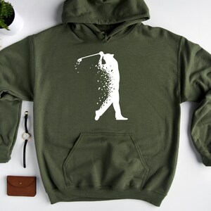 Op de afbeelding: Een groene hoodie met een wit silhouet van een golfer die een club zwaait. De golfer is gemaakt van kleine witte stippen.