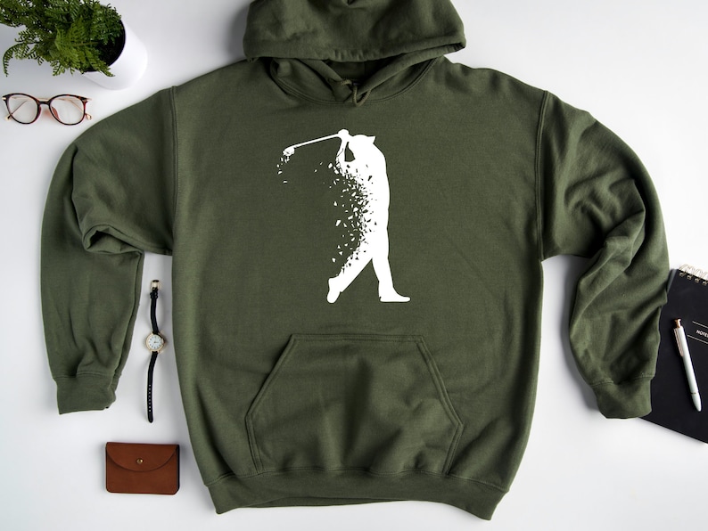 Op de afbeelding: Een groene hoodie met een wit silhouet van een golfer die een club zwaait. De golfer is gemaakt van kleine witte stippen.