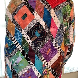 May include: A colorful patchwork jacket with a diamond pattern. The jacket is made of various fabrics in shades of pink, blue, green, purple, and brown. The fabric is sewn together in a geometric pattern.