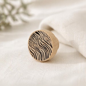 May include: A round wooden cabinet knob with a zebra stripe design. The knob is made of light-coloured wood and features black stripes. The knob is a decorative element for furniture and home decor.