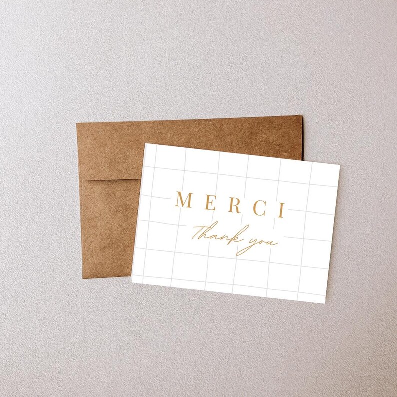 May include: A white card with a grid pattern and the words "MERCI" and "Thank you" in gold lettering.