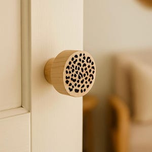 Könnte beinhalten: Ein Holztürknauf mit natürlicher Oberfläche und kreisförmigem Design. Die Vorderseite des Knaufs weist ein Muster aus schwarzen Punkten auf. Der Knauf ist an einer weißen Tür montiert.