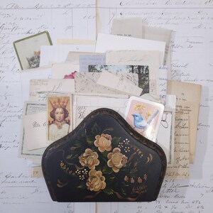 Pode incluir: Um porta-cartas vintage preto pintado &agrave; m&atilde;o com um design floral, cheio de cartas antigas, cart&otilde;es e ef&ecirc;meras. O porta-cartas tem uma forma curva e &eacute; adornado com rosas creme.
