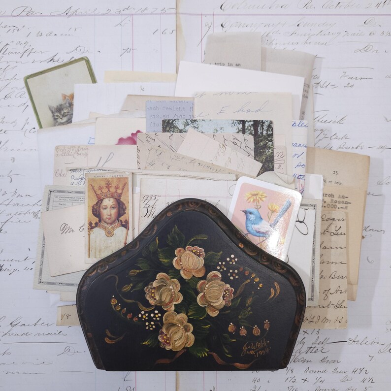 Pode incluir: Um porta-cartas vintage preto pintado &agrave; m&atilde;o com um design floral, cheio de cartas antigas, cart&otilde;es e ef&ecirc;meras. O porta-cartas tem uma forma curva e &eacute; adornado com rosas creme.