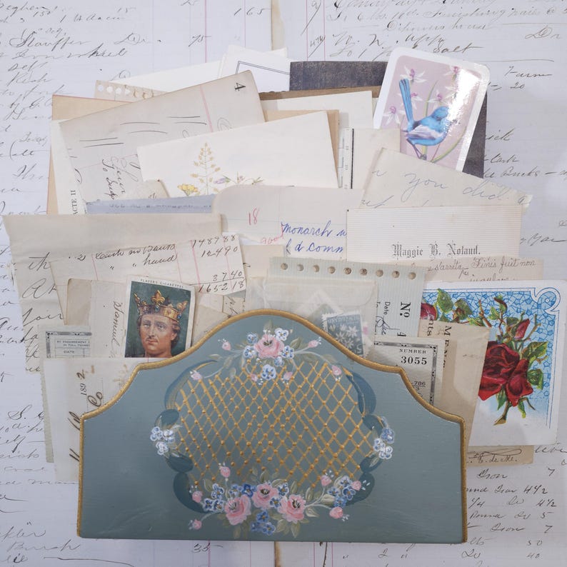 Pode incluir: Um organizador de mesa em estilo vintage em um tom azul suave, adornado com detalhes dourados e motivos florais. O organizador cont&eacute;m uma cole&ccedil;&atilde;o de pap&eacute;is, cart&otilde;es e ef&ecirc;meras antigas, criando uma est&eacute;tica nost&aacute;lgica. O design inclui uma frente decorativa com um padr&atilde;o de treli&ccedil;a.