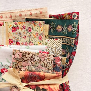 May include: A bundle of floral fabric scraps in various patterns and colors, including red, pink, green, and cream. The fabrics are tied together with a beige ribbon, showcasing a variety of floral designs, stripes, and textures. Ideal for quilting or crafting projects.
